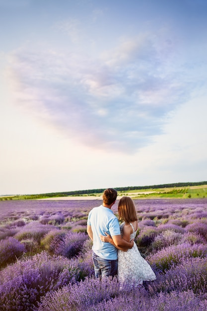 Foto casal apaixonado olha a paisagem pitoresca. campo de lavanda. pôr do sol. nuvem em forma de coração.