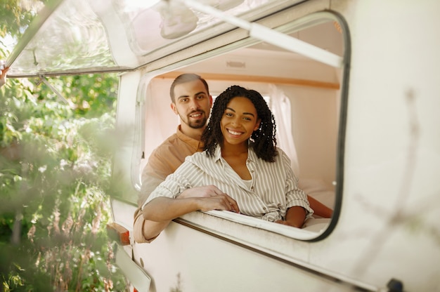 Casal apaixonado parece pela janela do trailer, acampando em um trailer. homem e mulher viajando em van, férias românticas em motorhome, lazer para campistas em carro de camping