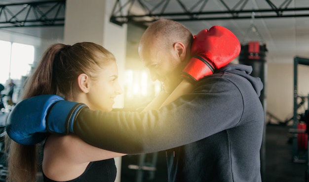 Foto casal apaixonado se abraça em luvas de boxe e olha nos olhos um do outro no ginásio.