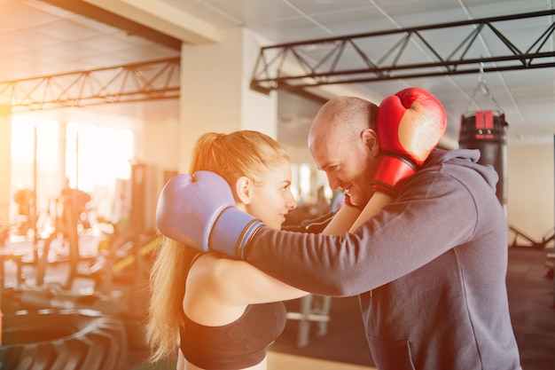 Casal apaixonado se abraça em luvas de boxe e olha nos olhos um do outro no ginásio.