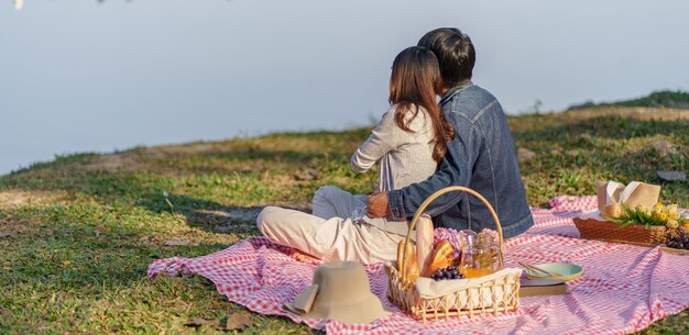 Casal apaixonado se abraçando aproveitando a hora do piquenique no parque ao ar livre Casal feliz de piquenique relaxando junto com a cesta de piquenique