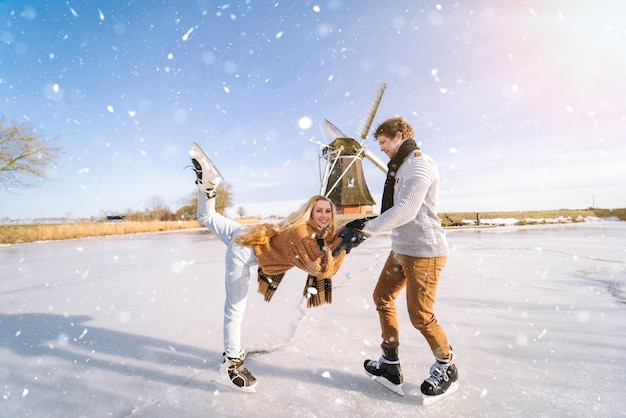 Casal apaixonado se divertindo no gelo em uma paisagem típica holandesa com uma mulher e um homem do moinho de vento patinando no gelo