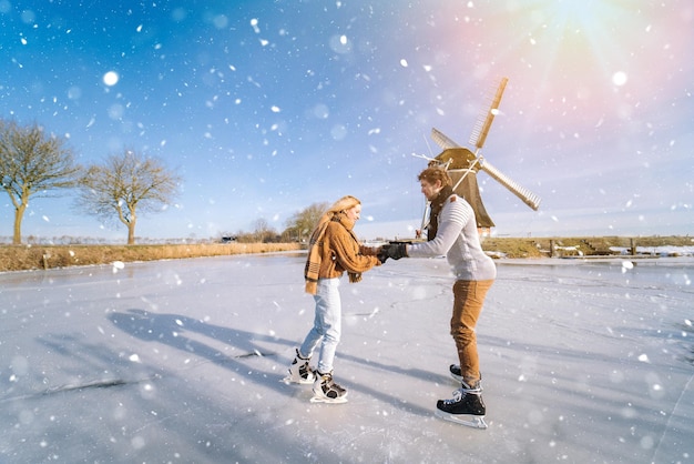 Casal apaixonado se divertindo no gelo em uma paisagem típica holandesa com uma mulher e um homem do moinho de vento patinando no gelo