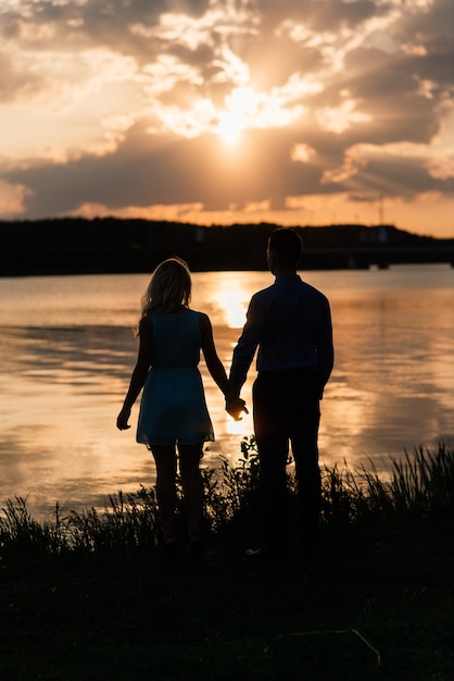 Casal apaixonado silhueta de luz de fundo no pôr do sol laranja do lago, romântico.