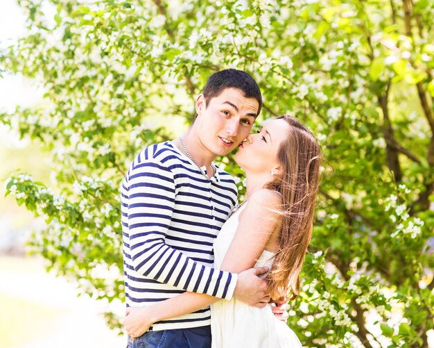 Casal apaixonado sob galhos florescendo dia de primavera. Jovem adulto morena homem e mulher beijando no jardim de árvores de maçã ou cereja de flor fresca. beijo doce