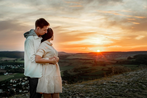 casal apaixonado, um cara e uma garota ficam em uma montanha ao pôr do sol e olham para o pôr do sol