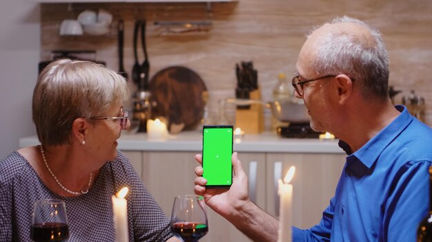 Casal aposentado sênior segurando telefone de tela verde no jantar