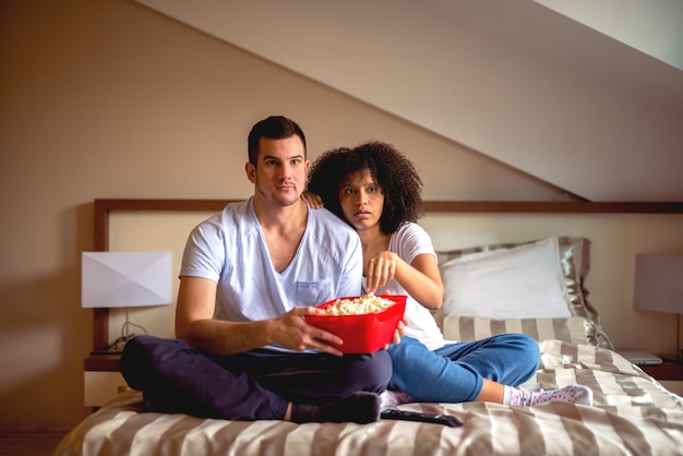 Foto casal aproveitando o tempo de compartilhar em casa com filme e pipoca.