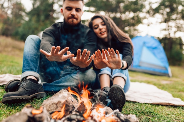 Casal aquecendo as mãos perto da fogueira