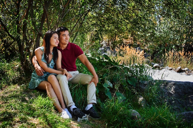 Casal asiático apaixonado por homem cazaque e mulher tailandesa acaricia, abraça e beija em uma floresta de verão. Piquenique romântico na natureza