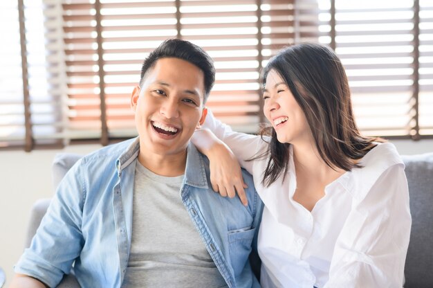 Casal asiático apaixonado, sorrindo e rindo no sofá em casa