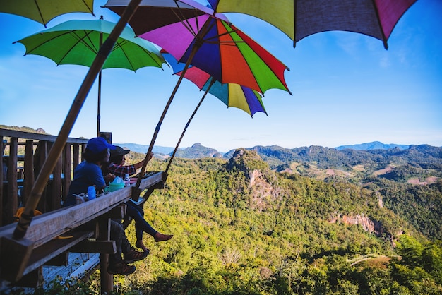 Foto casal asiático de turistas sentado a comer macarrão na plataforma de madeira e olhando a vista panorâmica das montanhas da bela natureza em ban jabo, mae hong son, thialand.