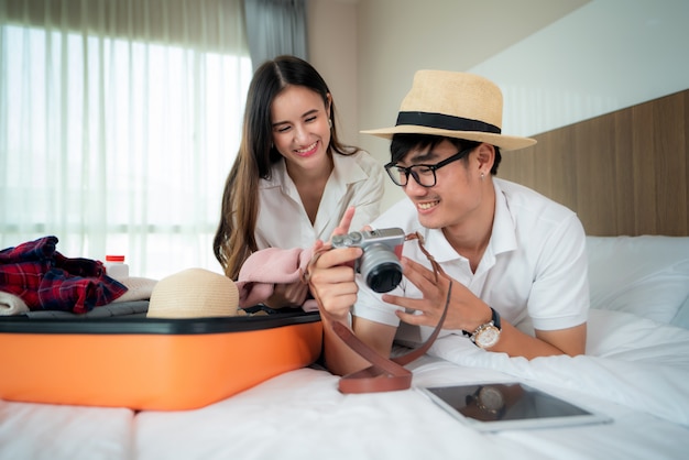 Casal asiático feliz desembalar a mala na cama no quarto quando chegarem no quarto de hotel e mentir e olhar a foto em viagem viagem para a câmera. conceito de estilo de vida asiático viagens mochileiros.