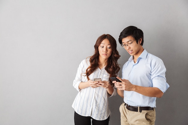 Casal asiático feliz isolado, usando telefones celulares