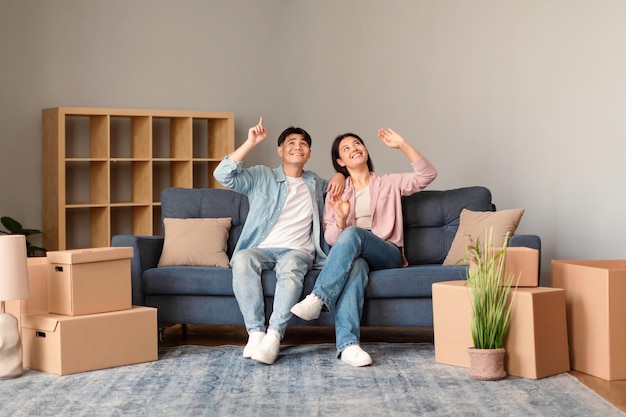Casal asiático planejando reforma de casa em meio a caixas no sofá interno