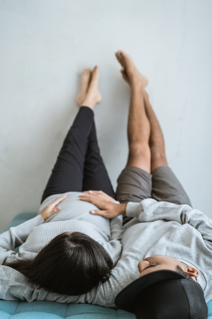 Casal asiático relaxando no sofá com as mãos segura da esposa barriga grávida