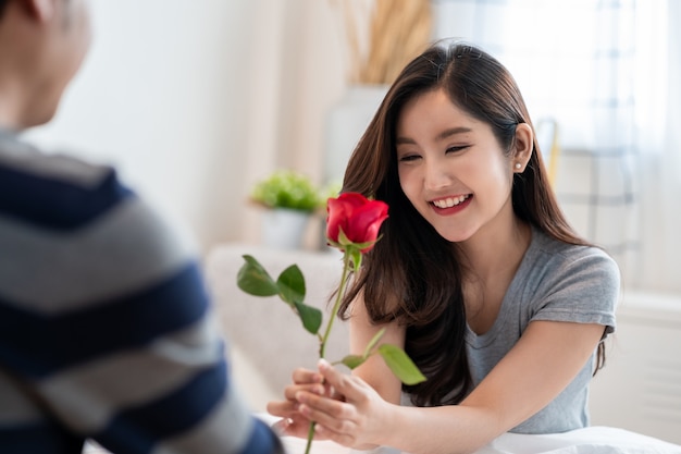 Casal asiático romântico no quarto, um homem dando uma rosa para uma linda mulher e os dois beijando uma linda rosa com amor e felicidade, lindo casal asiático elegante está abraçando e sorrindo no quarto