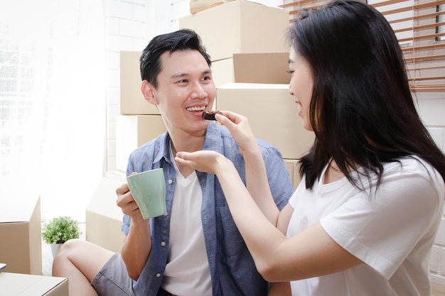 Casal asiático sorridente feliz se mudando para uma nova casa A esposa alimenta o marido com lanches. Conceito de família, o início de uma nova vida.