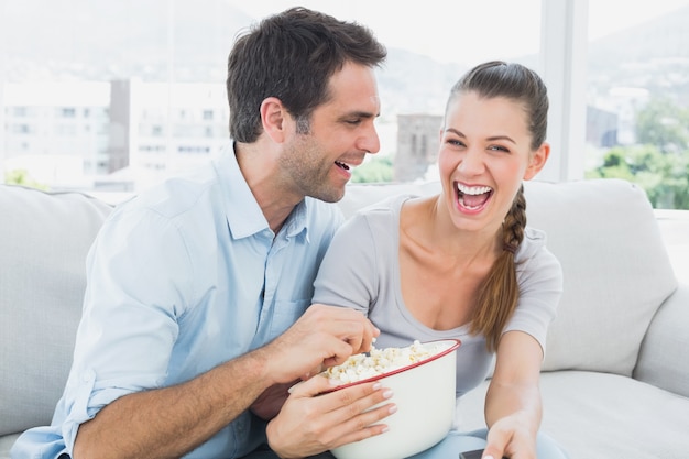 Casal assistindo filme engraçado no sofá com uma tigela de pipoca