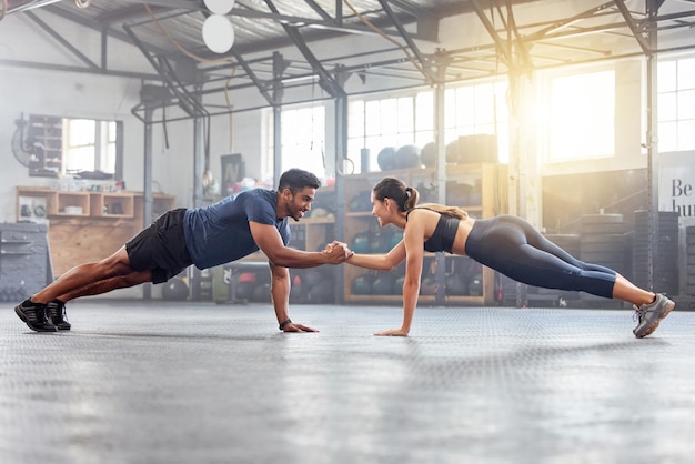 Casal ativo de mãos dadas para apoio na prancha de flexão e treinamento de equilíbrio durante treino de fitness e exercício em uma academia Atletas fortes e aptos esportivos, ajudando no desafio de bem-estar do peso corporal