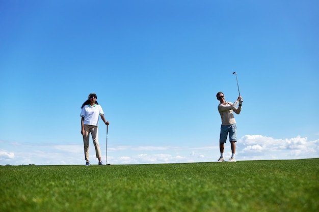 Casal ativo jogando golfe no campo contra o céu azul