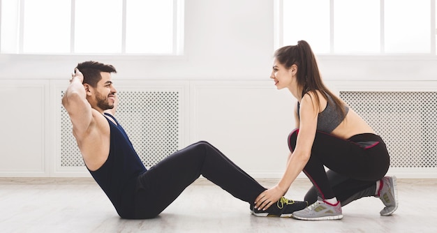 Casal atlético ajudando um ao outro com exercícios de abdominais em estúdio claro, panorama, espaço de cópia