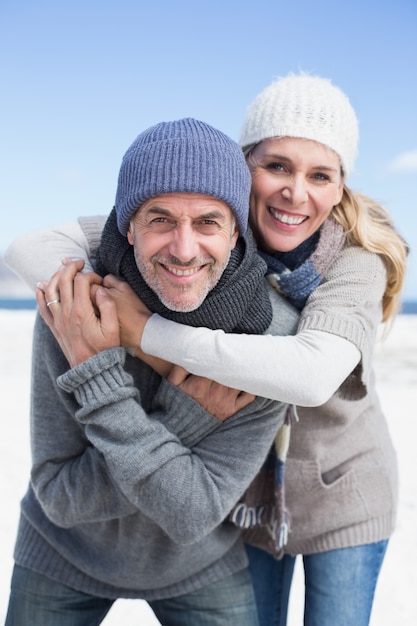 Casal atraente abraçando e sorrindo para a câmera na praia com roupas quentes