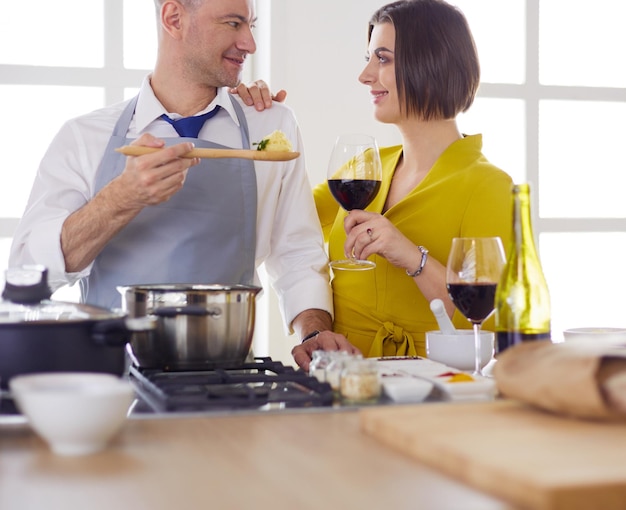 Casal atraente apaixonado por cozinhar e abre o vinho na cozinha enquanto cozinha o jantar para uma noite romântica