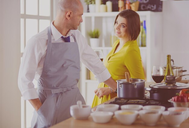 Casal atraente apaixonado por cozinhar e abre o vinho na cozinha enquanto cozinha o jantar para uma noite romântica