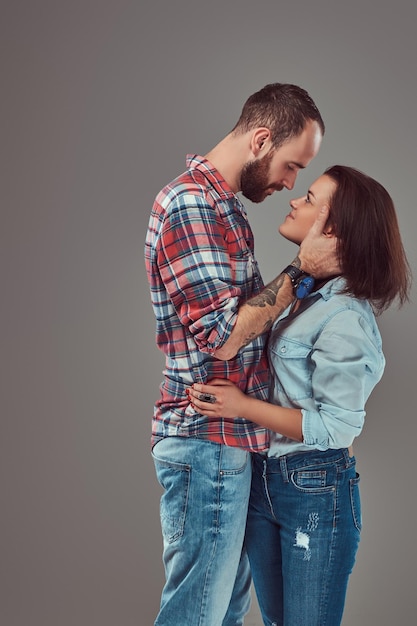 Casal atraente, homem barbudo e menina morena abraçando em um estúdio. Isolado em um fundo cinza.