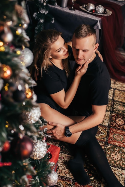 Casal atraente no Natal em casa perto de uma árvore de Natal, abraçando-se. Foto de ano novo de um cara e uma garota no interior de um ano novo, uma casa decorada aconchegante.
