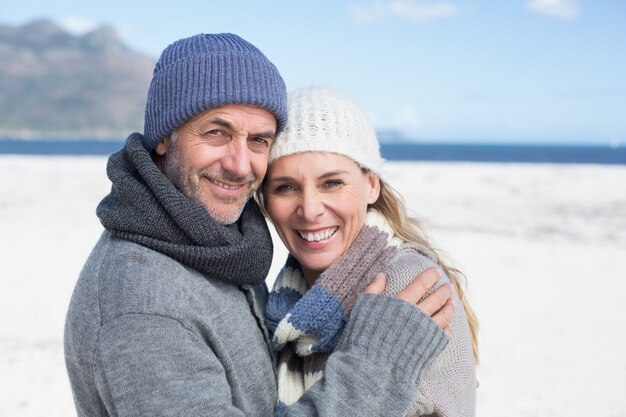 Casal atraente sorrindo para a câmera na praia com roupas quentes