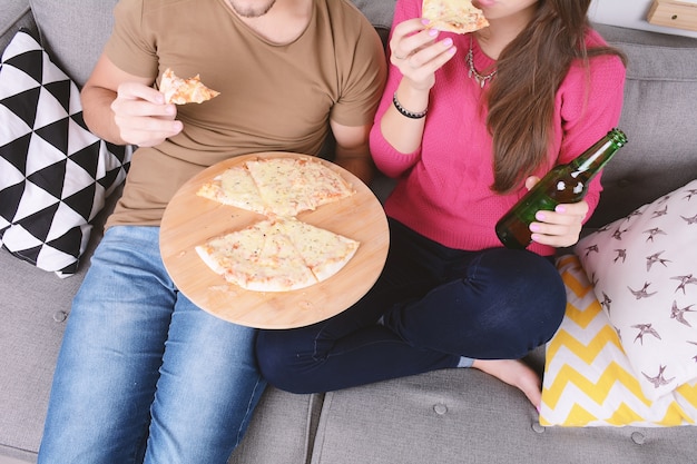 Casal bebendo cerveja e comendo pizza.