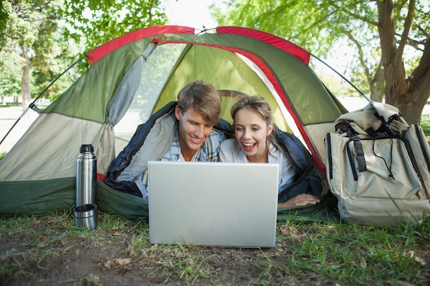 Casal bonito deitado na sua tenda usando laptop