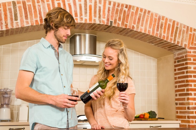 Casal bonito, desfrutando de um copo de vinho e lendo a garrafa na cozinha