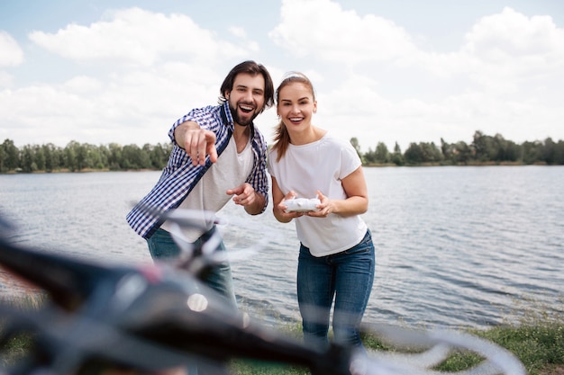 Casal bonito e feliz está juntos e lançando o drone. É controlado pelo painel de controle. Homem está apontando no zangão. Eles estão animados.