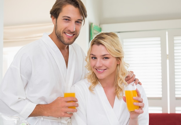 Casal bonito em roupões de banho sorrindo para a câmera juntos, tomando café da manhã