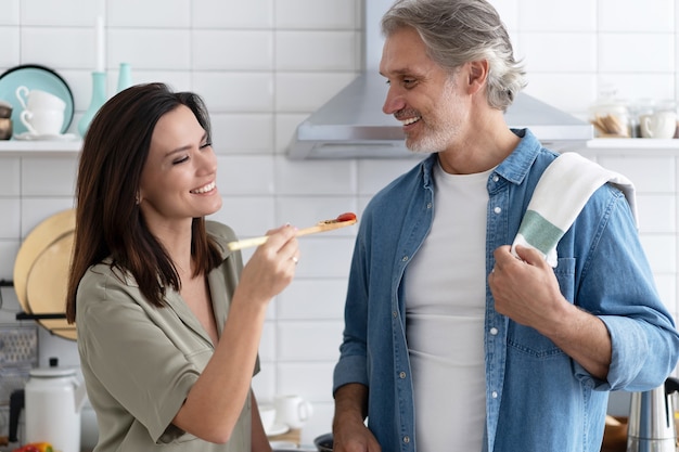 Casal bonito. Mulher alimentando o marido e sorrindo enquanto cozinha na cozinha em casa.