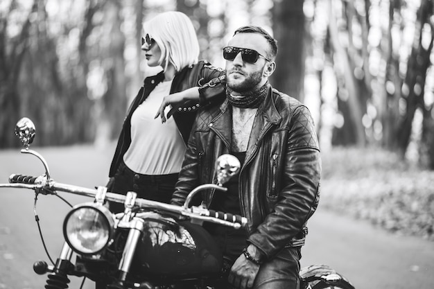 Foto casal bonito perto de moto na estrada na floresta com fundo blured