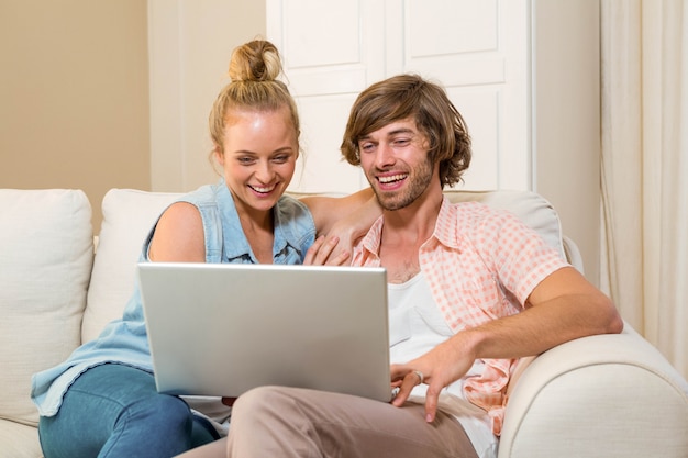 Casal bonito usando laptop sentado no sofá na sala de estar