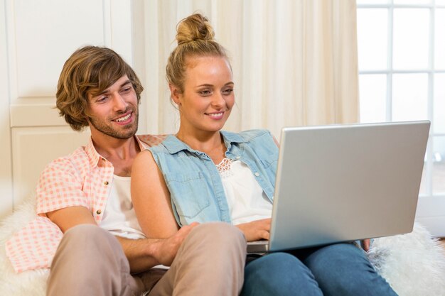 Casal bonito usando laptop sentado no sofá na sala de estar