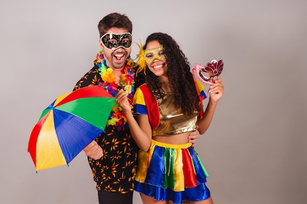 Casal brasileiro com roupas de carnaval segurando máscara e guarda-chuva de acessórios de carnaval