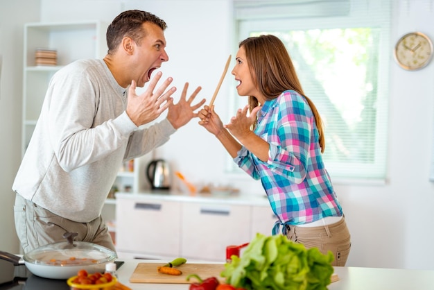 Casal bravo atraente discutindo, brigando e gritando um com o outro na cozinha doméstica.