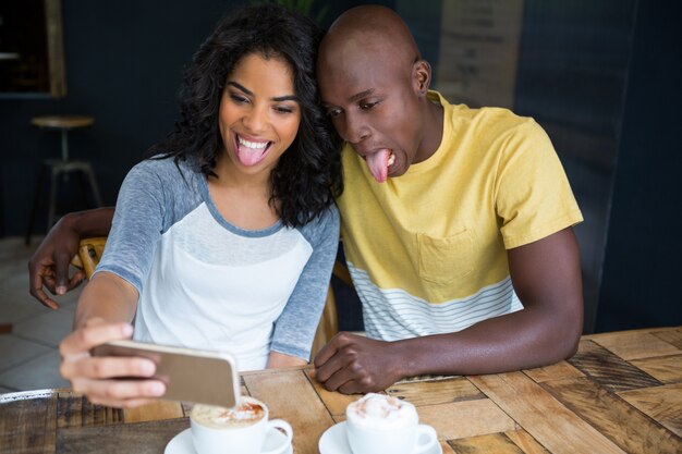 Casal brincalhão fazendo caretas enquanto tira uma selfie na cafeteria