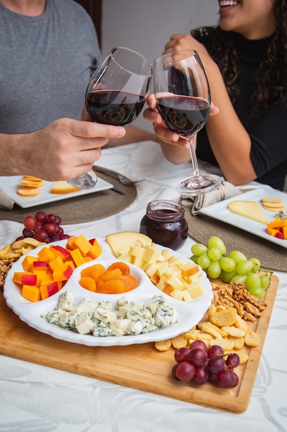 Foto casal brindando com vinho e queijo no jantar. foco em queijos