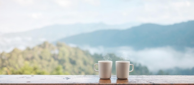 Casal caneca branca de café quente ou chá na mesa de madeira pela manhã com fundo de montanha e natureza