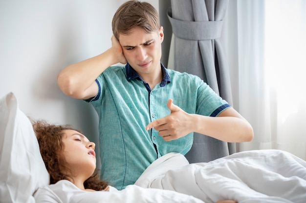 Casal caucasiano de pijama roncar e dormir mal no quarto. seus ouvidos de bloqueio com as mãos.