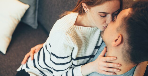 Casal caucasiano encantador se beijando no sofá em um dia ensolarado de fim de semana