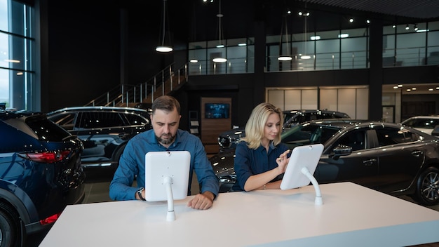 Foto casal caucasiano escolhe um carro em uma concessionária de carros em tablets digitais