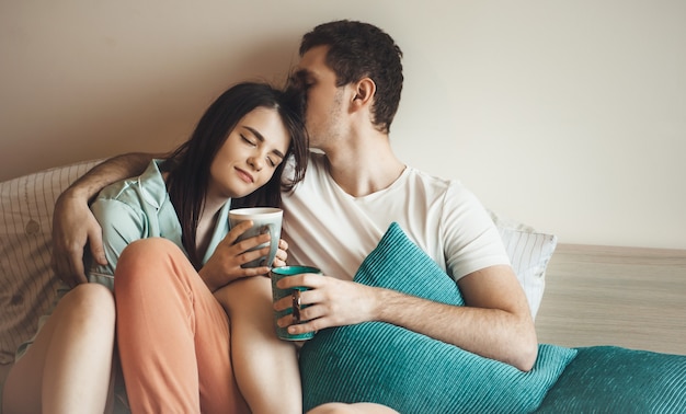 Casal caucasiano feliz na cama tomando chá pela manhã, abraçando e curtindo o tempo